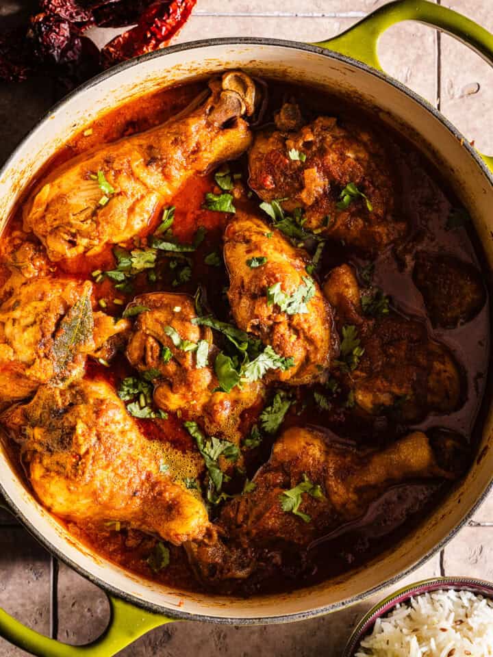 Cooked chicken curry in a dutch oven served with rice and chili peppers.