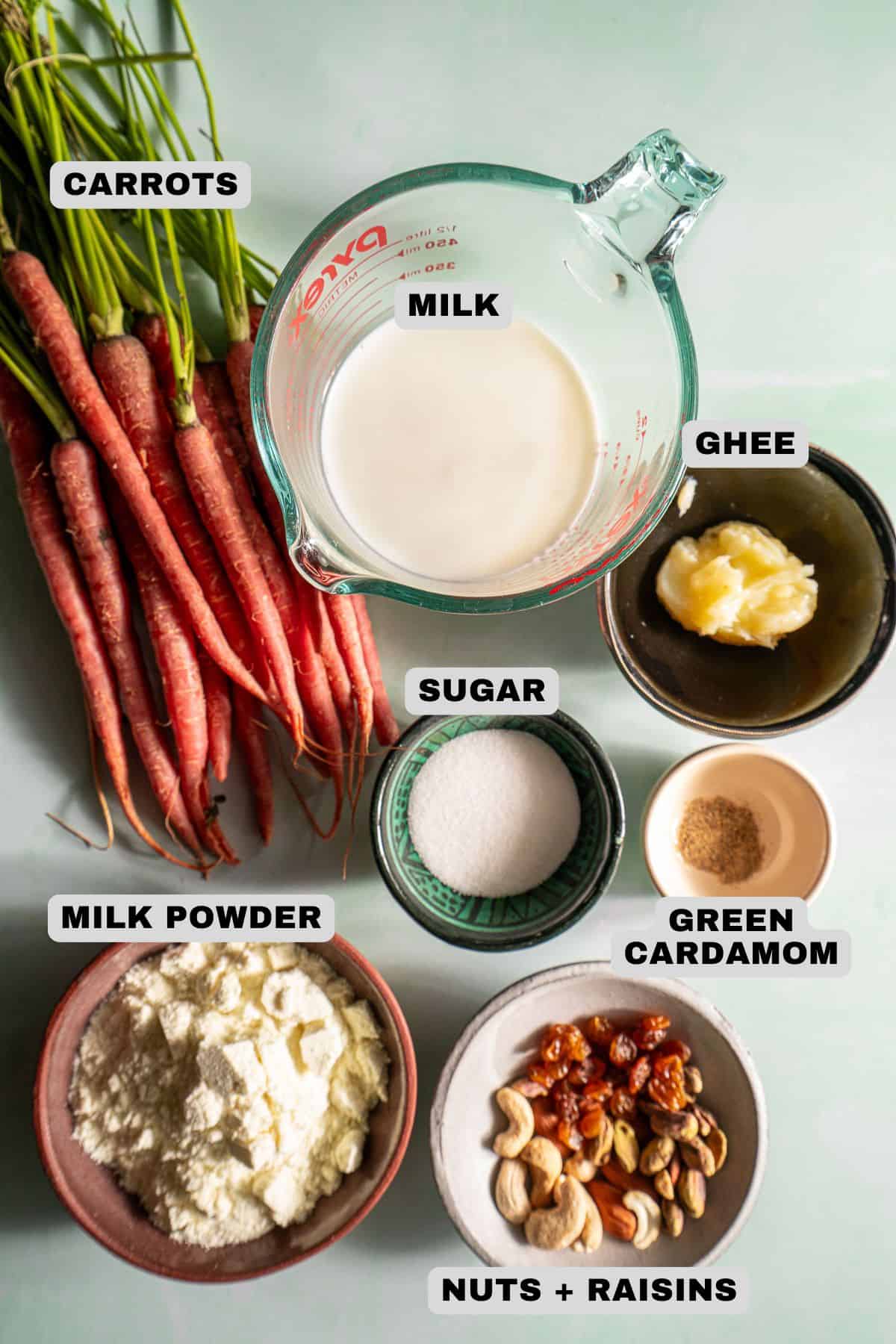 Carrots, milk, ghee, sugar, milk powder, green cardamom, nuts + raisins ingredients with labels.