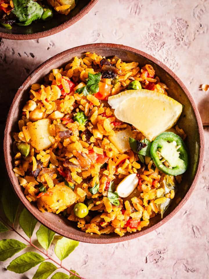 Flavorful vegetable poha with spices, lemon, jalapeno slice, and fresh herbs.