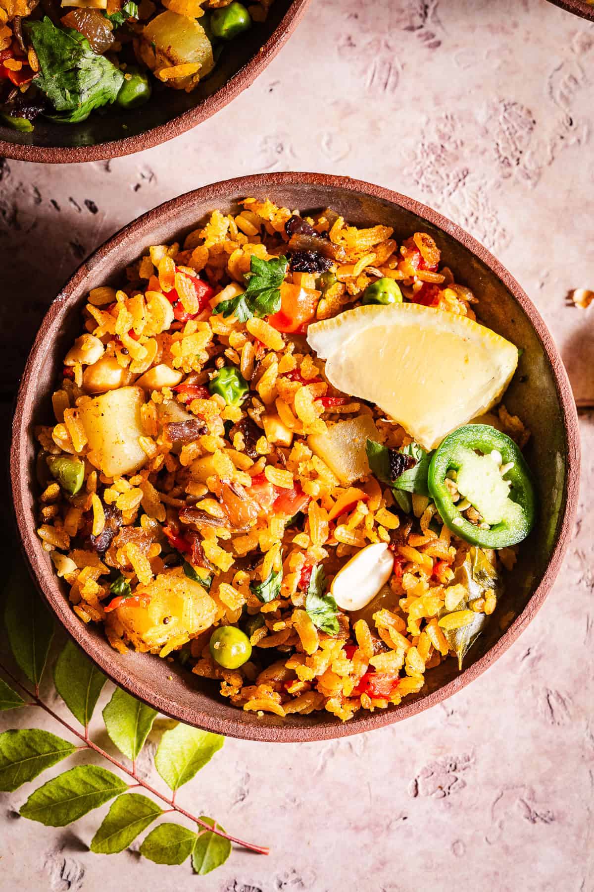 Flavorful vegetable poha with spices, lemon, jalapeno slice, and fresh herbs.
