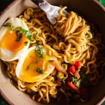 Spicy masala noodles topped with a soft-boiled egg, fresh herbs, and vegetables in a rustic bowl.