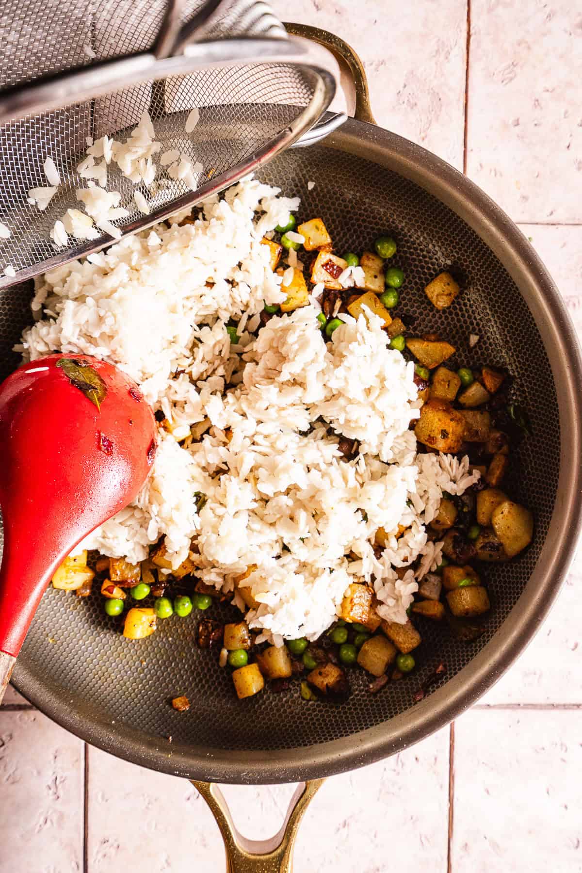 Poha rice being prepared with mixed vegetables and spices in a kitchen strainer.