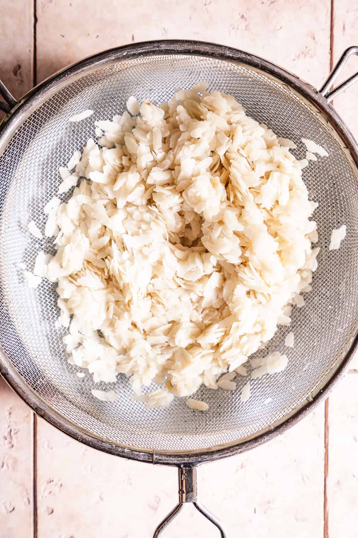 Poha rinsed in a metal strainer, ready for cooking or serving.