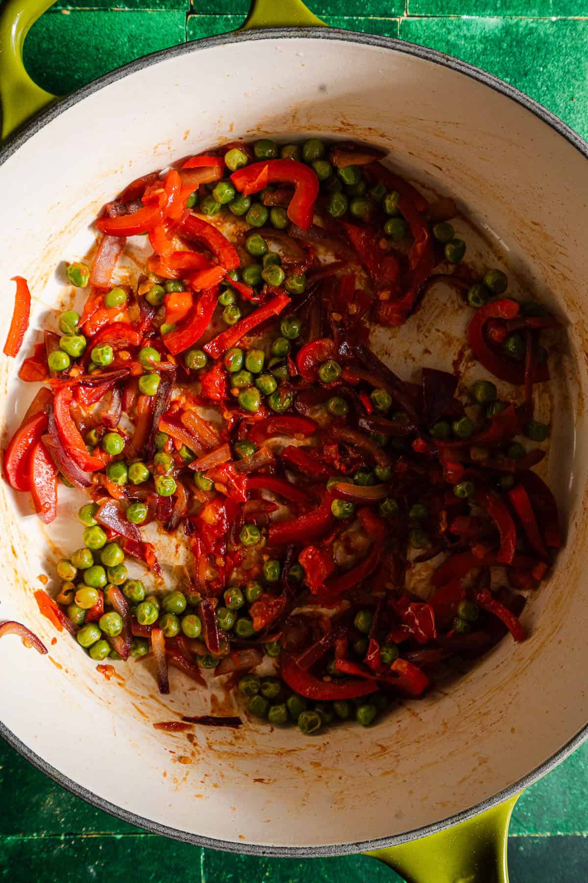Sauteed bell peppers, onions, tomatoes, and peas in a pot.
