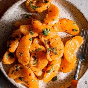 Orange chaat in a plate with a fork.