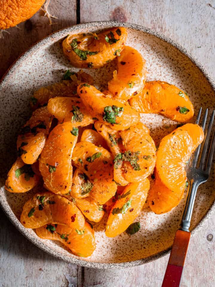 Orange chaat in a plate with a fork.